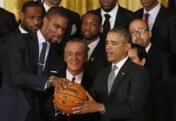 Chris Bosh le entrega un balón firmado al presidente Obama. LeBron y Wade le observan.