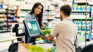 Beautiful friendly customer at checkout smiling at male cashier while he scans products in a supermarket **DESIGN ON SCREEN WAS MADE FROM SCRATCH BY US**