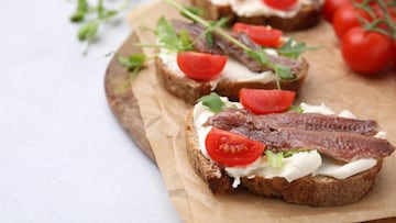 Delicious bruschettas with anchovies, tomatoes, microgreens and cream cheese on white table, closeup. Space for text