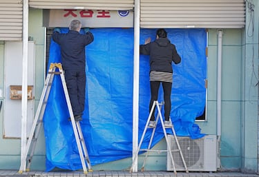 Personas cubren los cristales rotos con una sábana azul en un salón de belleza en Hachinohe.