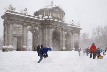 Varias personas caminan junto a la Puerta de Alcalá de Madrid.