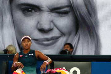 Naomi Osaka descansa en el banco y tras ella un cartel publicitario del torneo australiano.