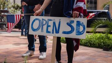 A woman holds a US flag an an &quot;Open SD&quot; sign during a rally in downtown San Diego against California&#039;s stay at home order to prevent the spread of the novel coronavirus, which causes COVID-19, on April 18, 2020. - Hundreds protested Saturda