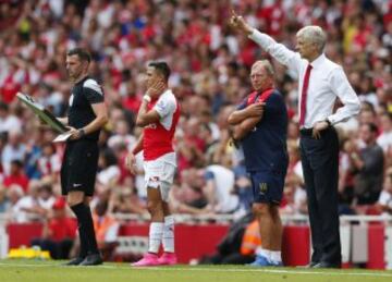 Alexis Sánchez espera por ingresar a la cancha, mientras Arsene Wenger da instrucciones.