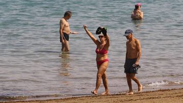 Varias personas toman el sol, pasean y se bañan en la playa.