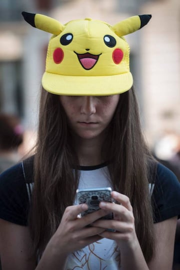 A girl sporting a "Pikachu" hat uses the Pokemon Go application on her mobile as she participates in a mass gathering in Madrid on July 28, 2016.  Over 5,000 people have signed up to take part in a mass Pokemon Go hunt at Madrid's central Puerta del Sol square which seeks to set a world record for greatest number of people playing the augmented reality game in the same place at the same time. / AFP PHOTO / PEDRO ARMESTRE