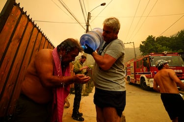 Un hombre ayuda a un residente a refrescarse con agua embotellada.