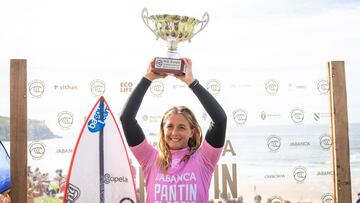 Leticia Canales con el trofeo de campeona de Europa de surf de la WSL en Pantín, con un fotocall y la playa al fondo.