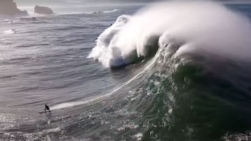 Una ola gigante rompiendo sobre un surfista en Praia do Norte (Nazar&eacute;, Portugal), con un jet ski y los acantilados al fondo. 