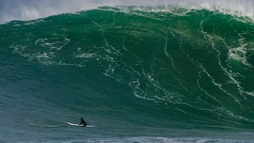 Una ola grande rompe en La Vaca (Cueto, Santander, Cantabria) mientras tres surfistas subidos a sus tablas de surf se lo miran y uno de ellos señala la ola con su dedo.