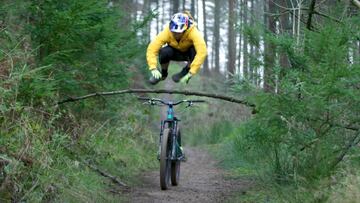 El piloto de mountain bike Danny MacAskill, vestido de amarillo con el casco Red Bull, saltando sobre una rama mientras su bici pasa por debajo en la parte del Real MTB de los X Games. 