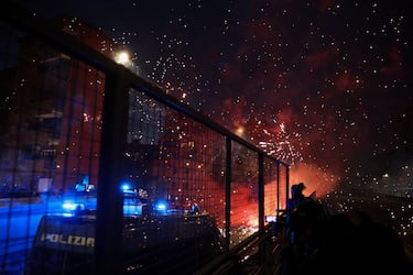 Una persona usa una cámara junto a un vehículo policial, mientras explotan fuegos artificiales mientras los manifestantes los usan contra las fuerzas del orden al intentar bloquear una carretera que conduce al Santa Giulia Arena, el día de una protesta contra el impacto ambiental, económico y social de los Juegos Olímpicos de Invierno Milano-Cortina 2026.