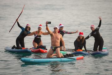 Surferos, ataviados con gorros de Pap Noel, se hacen un selfie sobre sus tablas dentro del mar.
