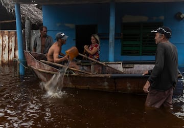 Un hombre saca agua de una embarcación mientras habla con vecinos tras el paso del huracán Helene en Guanimar, provincia de Artemisa, Cuba.