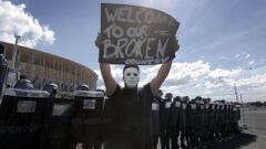 Un joven sostiene una pancarta frente a un grupo de agentes de polic&iacute;a antidisturbios, durante una protesta llevada a cabo horas antes del partido inagural de la Copa Confederaciones.