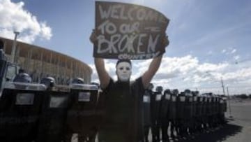 Un joven sostiene una pancarta frente a un grupo de agentes de polic&iacute;a antidisturbios, durante una protesta llevada a cabo horas antes del partido inagural de la Copa Confederaciones.