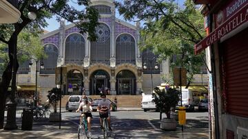 GRAFCVA7437. VALENCIA, 25/08/2020.- Dos turistas pasean en bicicleta ante el Mercado Central, en el centro histórico de Valéncia, en la última semana del mes de agosto. EFE/Manuel Bruque