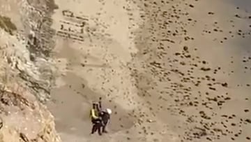 HELP escrito con piedras en una playa mientras rescatan a un kitesurfista.