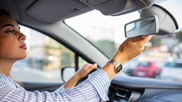 Brunette woman sitting on driver's seat and looking in the rear-view mirror. Girl adjusts the rear view mirror. Beautiful young lady looking back through the rear view mirror from the front seat of a car while reversing.