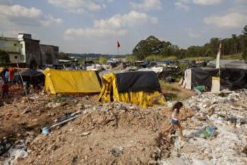Una niña camina en una área que fue ocupada por Integrantes del Movimiento de los Trabajadores Sin Techo (MTST) el pasado sábado situada a unos 4 kilómetros del estadio Arena Corinthians de Sao Paulo, una de las doce sedes del Mundial Brasil 2014 y que recibirá seis partidos del evento deportivo, entre ellos el inaugural del 12 de junio. De acuerdo con el movimiento, las familias que ocuparon el terreno, abandonado desde hace más de 20 años, vivían en áreas "de riesgo", "en favelas o sin condiciones para pagar el alquiler por culpa de la especulación inmobiliaria en la región, resultado de la construcción del estadio de apertura del Mundial".