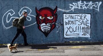 A man walks his dog past coronavirus COVID-19 themed graffiti in Glasgow on April 28, 2020. - More than 20,000 people have died in hospital in Britain with the new coronavirus, not including deaths in care homes and in the wider community, making it one o