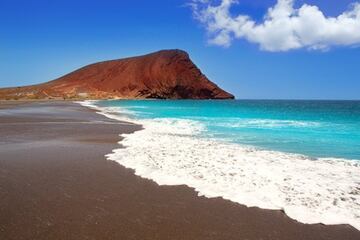 Un arenal recóndito en medio de una reserva natural de ensueño como es la de Montaña Roja con el típico paisaje volcánico que caracteriza a Canarias. Situada en El Médano, la Playa de la Tejita está prácticamente aislada de la zona residencial por lo que está garantizada la tranquilidad. Es uno de los arenales más salvajes y bonitos de Tenerife. 