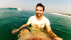 El doctor Nicholas Taylor, decano de la Facultat de Medicina de la Australian National Uniersity (ANU), se hace un selfie sobre su tabla de surf con una ola rompiendo al fondo y a la derecha la punta de una playa. 