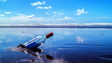 Una botella con mensaje varada en una playa, con olas al fondo. 