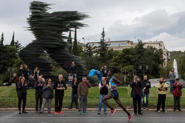 El atleta keniano Samuel Kalalei corriendo en la Maratón Clásica de Atenas delante de la estatua llamada "El corredor".
