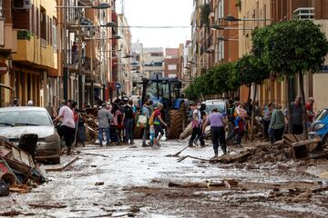 La gente se reúne para limpiar una calle cubierta de barro, tras las fuertes lluvias que provocaron inundaciones, en Sedaví, Valencia.