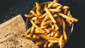 high angle shot of some appetizing french fries served in a white ceramic bowl, placed on a dark gray rustic wooden table