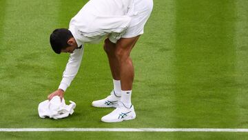 Novak Djokovic seca la hierba con una toalla durante su partido en Wimbledon contra Pedro Cachín.