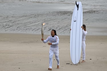 El surfista francés Edouard Delpero (izquierda) corre con la llama olímpica flanqueado por la surfista Zoe Grospiron (derecha).