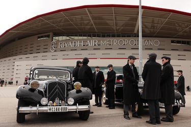 Personas con traje junto a coches inspirados en la serie de televisión Peaky Blinders a las afueras del estadio antes del partido.
