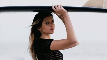 La modelo y surfista Anastasia Ashley con camiseta negra y una tabla de surf en la cabeza.