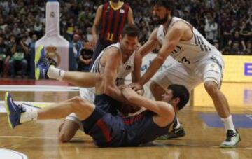 El alero del Real Madrid Rudy Fernández y su compañero el base Sergio Llull (d) luchan por el balón con el alero griego del FC Barcelona Konstantinos Papanikolaou, durante el partido correspondiente a la decimotercera jornada de Liga ACB que disputan frente al Real Madrid en el Palacio de los Deportes de Madrid.