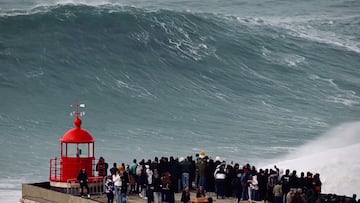 Ola gigante a punto de romper en Nazaré, con gente observando desde el faro, en el puente de diciembre 2025