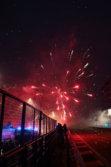 Agentes de policía se encuentran detrás de un vehículo, mientras los fuegos artificiales explotan mientras los manifestantes los usan contra las fuerzas del orden al intentar bloquear una carretera que conduce al Santa Giulia Arena, el día de una protesta contra el impacto ambiental, económico y social de los Juegos Olímpicos de Invierno Milano-Cortina 2026.