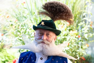 Acompañado de un penacho en el sombrero, luce una barba con extensiones horizontales que se abren como alas blancas. Además, presenta dos aros hechos con su bigote. 