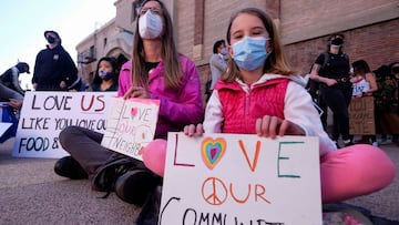 A woman and children wearing face masks sit on the pavement holding signs as they take part in a rally &quot;Love Our Communities: Build Collective Power&quot; to raise awareness of anti-Asian violence, at the Japanese American National Museum in Little T