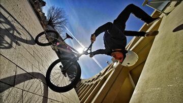 Tim Knoll practicando bike parkour en BMX haciendo la vertical sobre el manillar de su bici, con el sol al fondo.