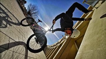 Tim Knoll practicando bike parkour en BMX haciendo la vertical sobre el manillar de su bici, con el sol al fondo. 