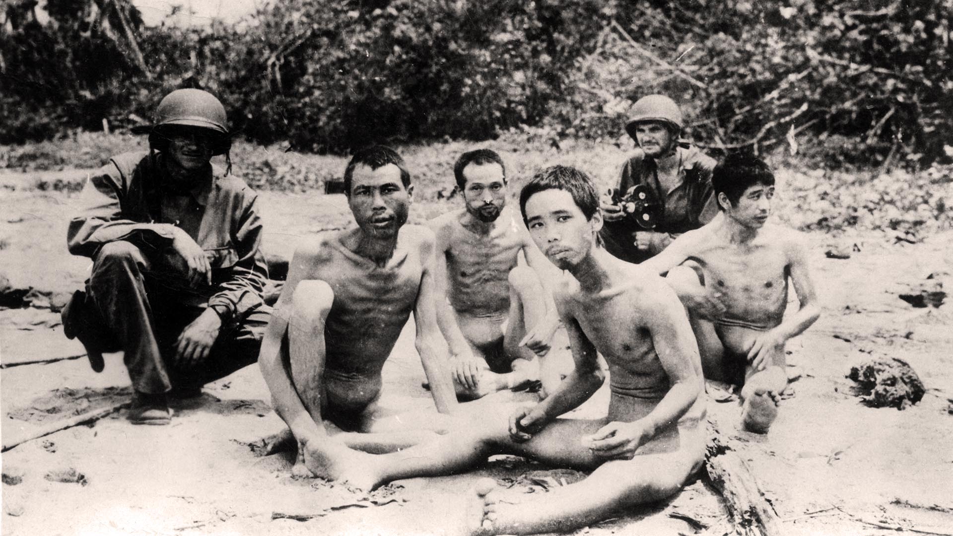 Dos soldados estadounidenses custodian a cuatro prisioneros de guerra japoneses enfermos que se habían rendido en una playa de Nueva Guinea, 1944.