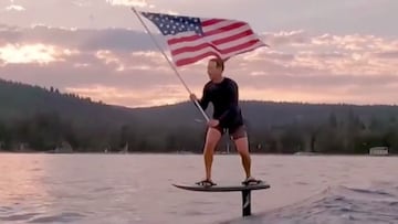 El fundador de Facebook, Mark Zuckerberg, ondeando la bandera de Estados Unidos mientras practica e-foil surfing en las aguas de algún lago.