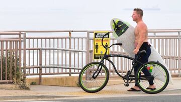 Un surfista en su bici lleva la tabla de surf en la playa de Newport Beach, California, durante las restricciones por coronavirus; y las nuevas medidas impuestas por el Gobernador para el 1 de mayo.