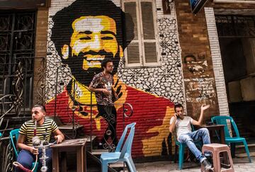 Ahmed Fathy, un artista egipcio de 26 a?os, desciende por una peque?a escalera de un caf¨¦ al aire libre en el centro de El Cairo. Tras ¨¦l el mural que pint¨® del rostro del delantero egipcio del Liverpool, Mohamed Salah.