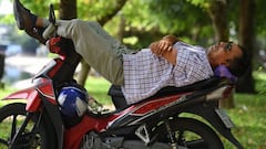 A man sleeps on a motorcycle under the trees in central Hanoi on August 9, 2022. (Photo by Nhac NGUYEN / AFP) (Photo by NHAC NGUYEN/AFP via Getty Images)