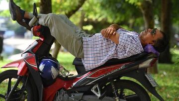 A man sleeps on a motorcycle under the trees in central Hanoi on August 9, 2022. (Photo by Nhac NGUYEN / AFP) (Photo by NHAC NGUYEN/AFP via Getty Images)