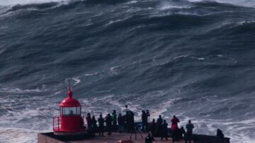 Varias personas en el faro de Nazaré (Portugal) observando una de las olas gigantes formándose justo delante.