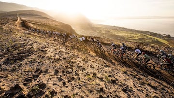 Participantes de la Cape Epic ruedan agrupados en un sendero de tierra.